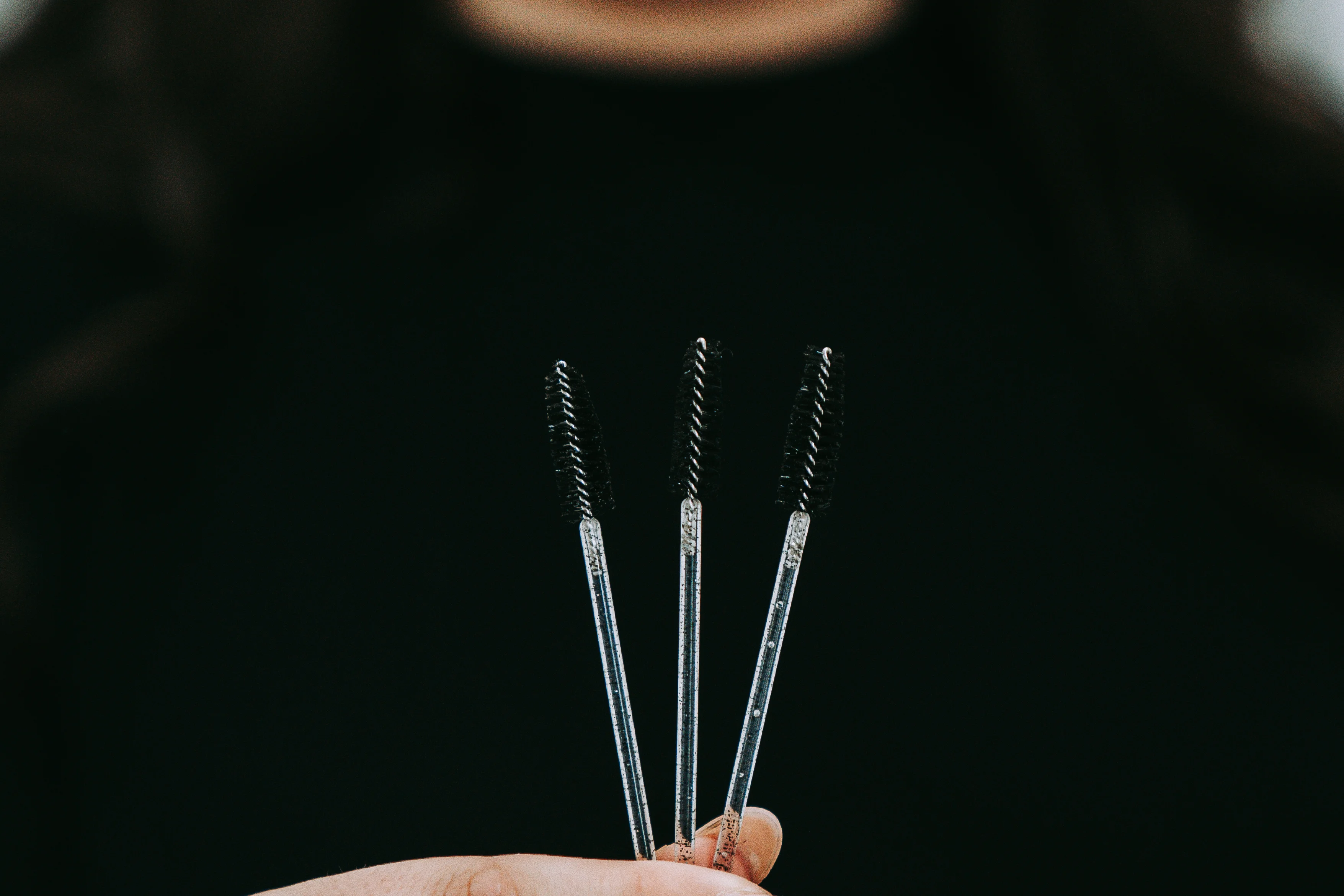 Three brow spoolie brushes held against a dark backdrop at the Roselli Cosmetologist salon