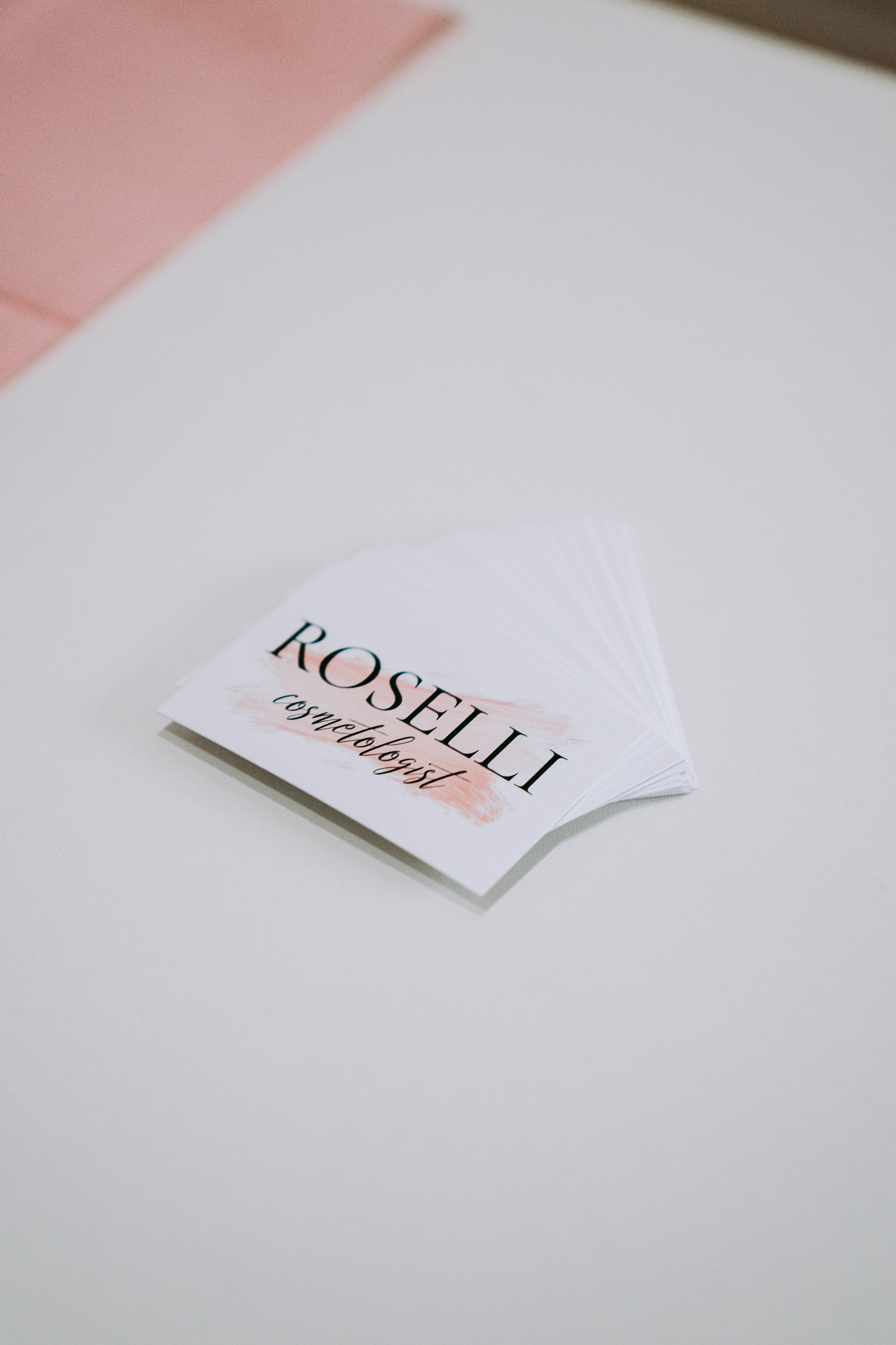 Roselli Cosmetologist branded business cards fanned on a soft white surface beside a blush pink cloth